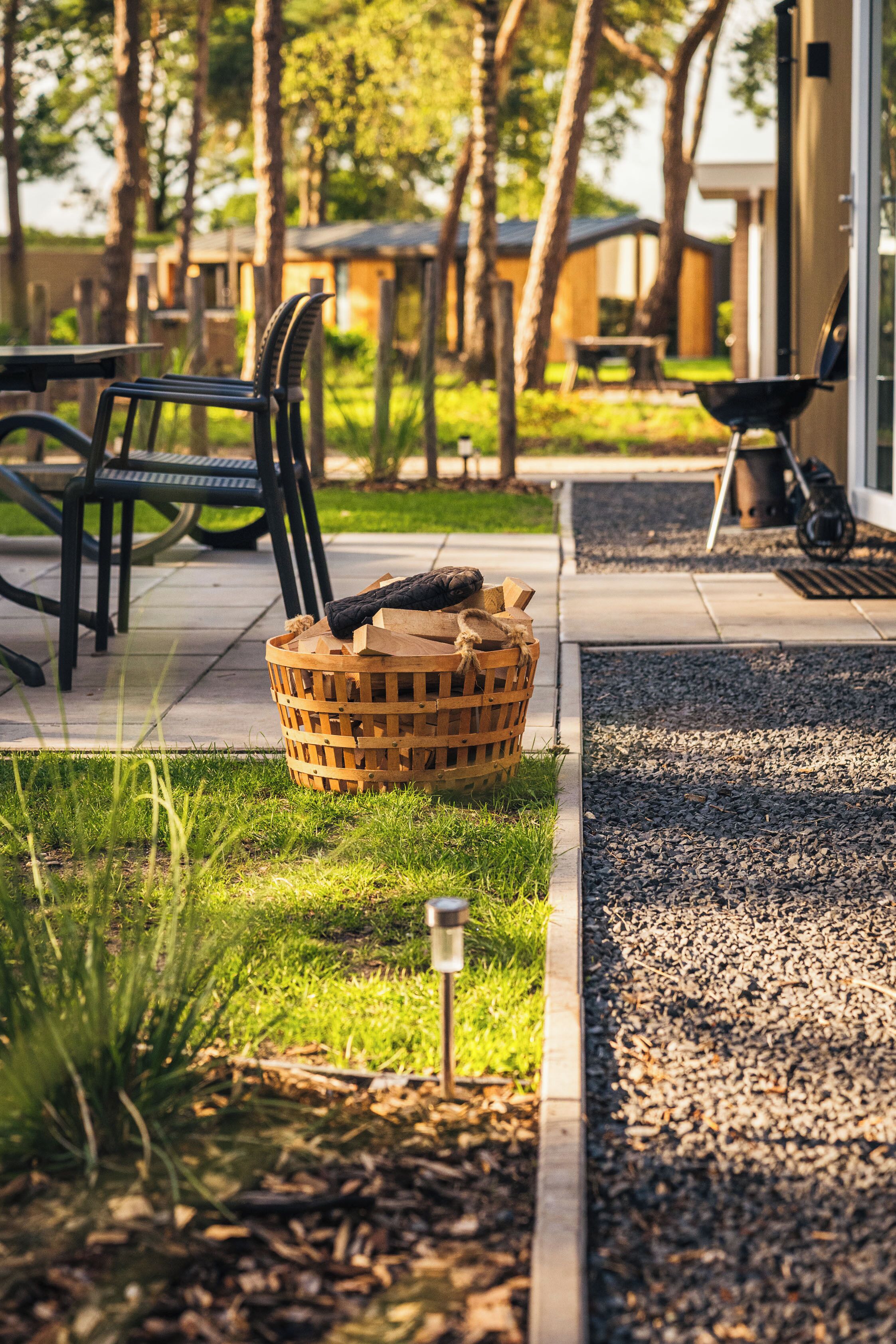 Ein Holzkorb auf einer Terrasse mit Gartenmöbeln und einem Grill.