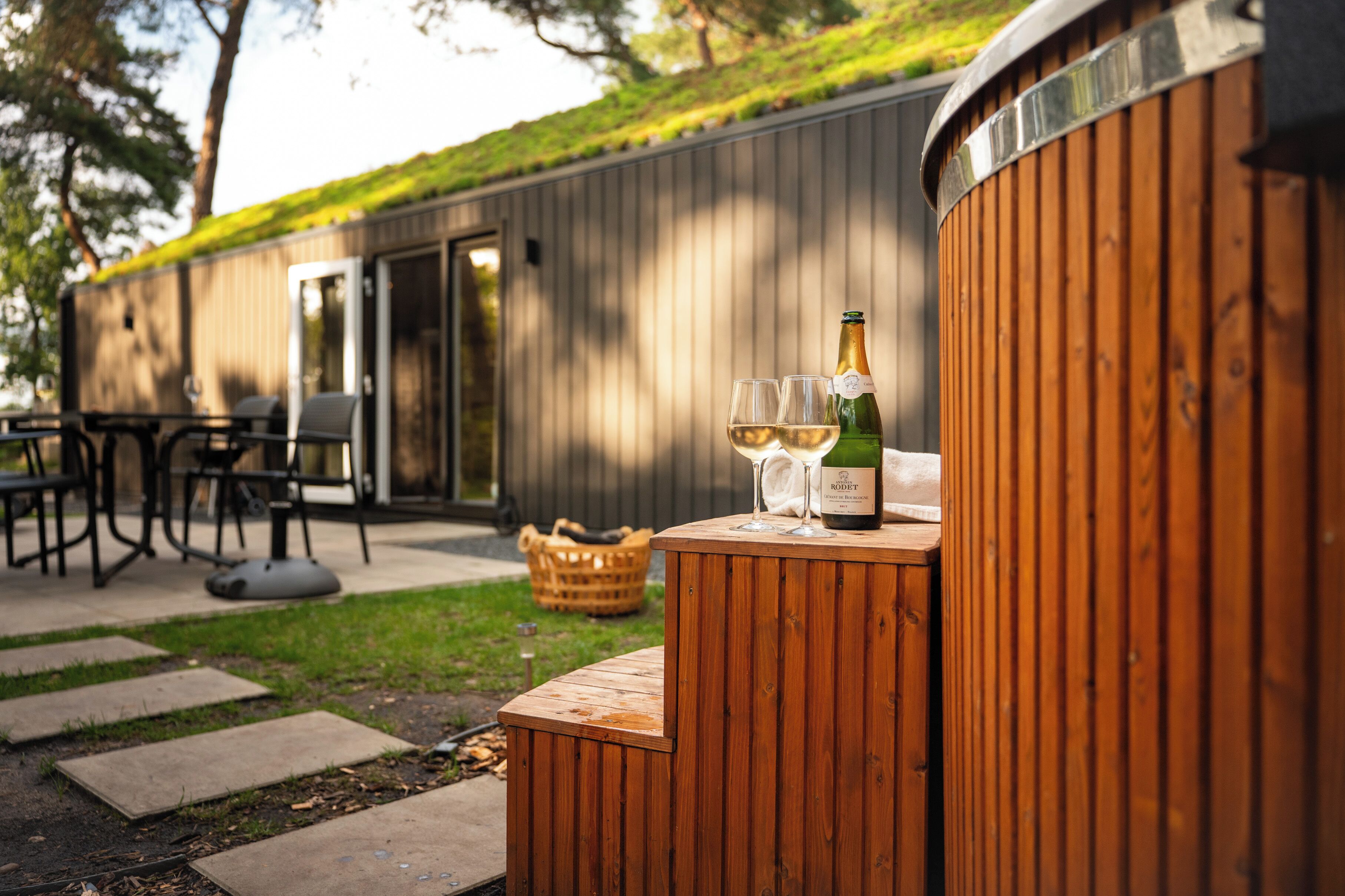 A wooden outdoor seating area with a bottle of wine and two glasses on a wooden table.