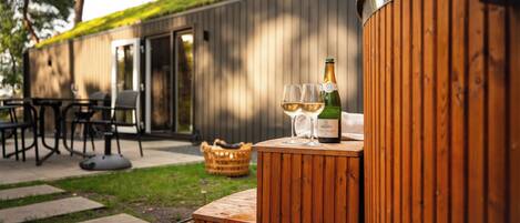 A wooden outdoor seating area with a bottle of wine and two glasses on a wooden table.