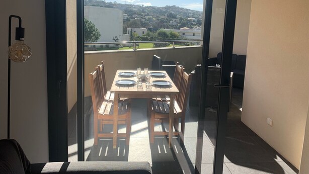 En balkon med et bord dækket til to personer, stole og udsigt over en by.