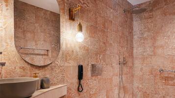 A bathroom with a large sink, a mirror, a towel rack, a shower, and a wall-mounted phone.