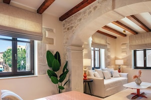 Una habitación con un arco de piedra, un sofá blanco, una mesita con un florero y una cama con colcha rosa.