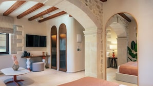 A spacious room with a large bed, a seating area with a table and chairs, and a television mounted on the wall. - La Montre Luxury Suites (Rethymno)