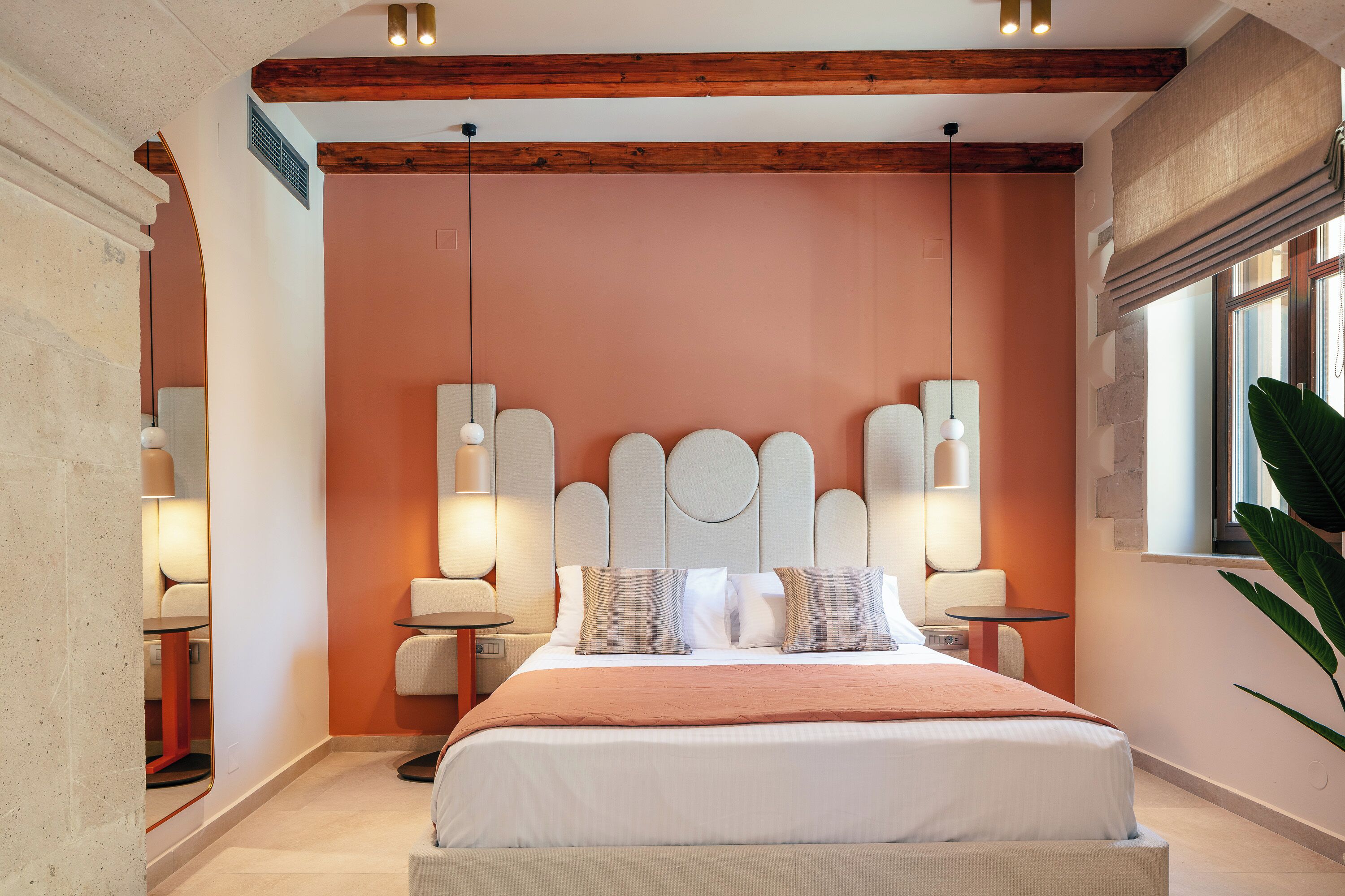 A modern bedroom with a large bed, two bedside tables, a headboard with circular designs, and a window with a view.