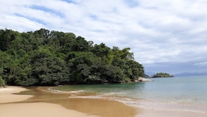 Una playa con aguas cristalinas, una orilla arenosa y abundante vegetación verde al fondo.