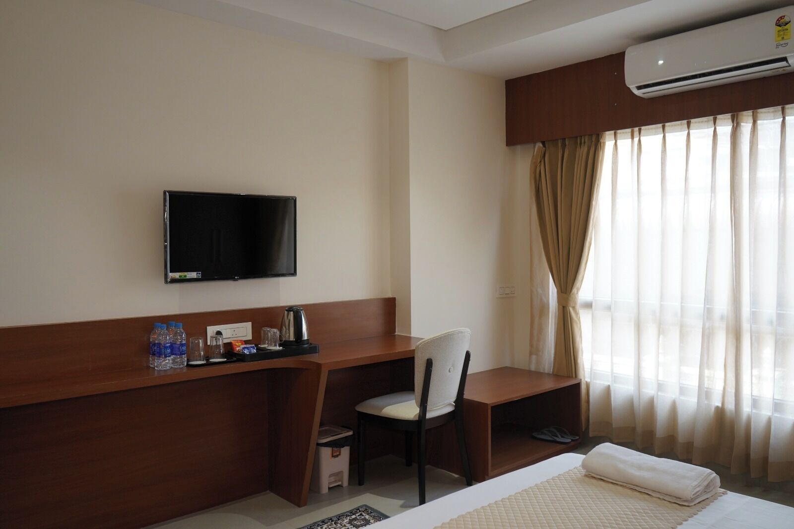 A hotel room with a bed, a desk with a chair, a television, and a window with curtains.