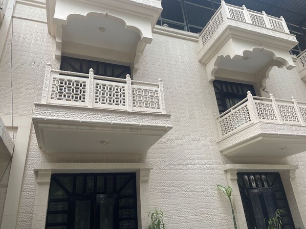 A building with white textured walls, black-framed windows, and ornate balconies with lattice railings. - Hotel Tourist Inn By Sagar (Jalpaiguri)
