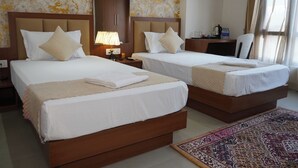 A hotel room with two beds, a nightstand with a lamp, a desk with a chair, and a patterned rug. - Hotel Tourist Inn By Sagar (Jalpaiguri)