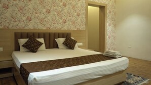 A neatly made bed with a brown bedspread and two patterned pillows, a wooden headboard, and floral wallpaper. - Hotel Tourist Inn By Sagar (Jalpaiguri)