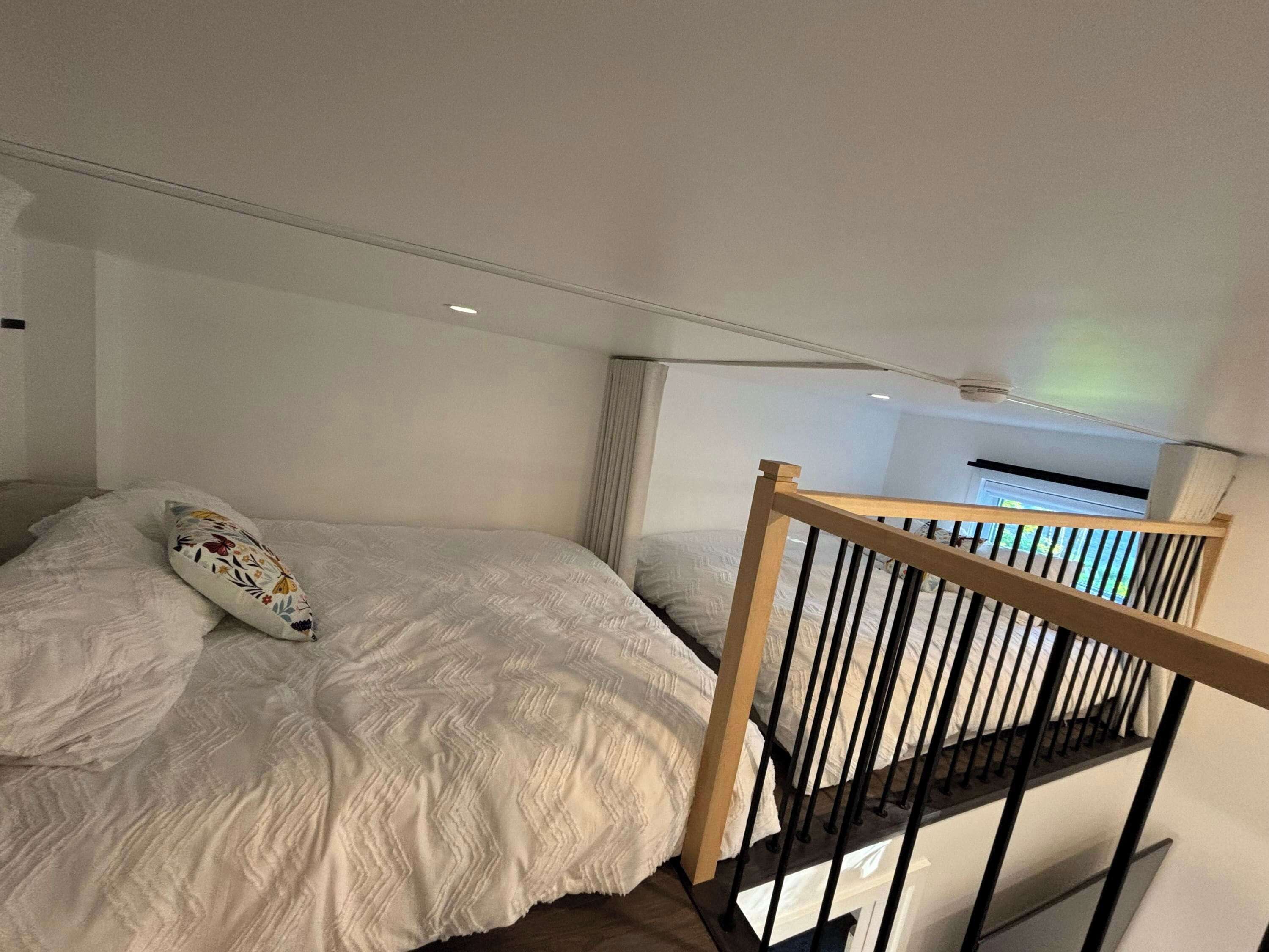 Une chambre à coucher avec un lit, une rambarde en bois et un appareil de climatisation fixé au plafond.