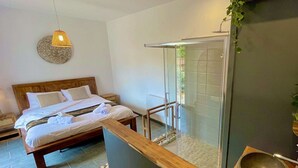 A modern hotel room with a wooden bed, a glass shower enclosure, and a small sink with a stone basin.
