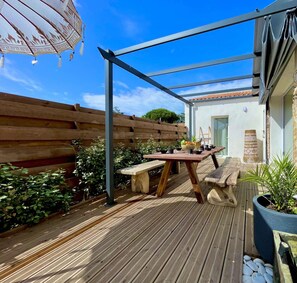 Eine Holzterrasse mit Tisch und Bänken, umgeben von einem Holzzaun und Blumentöpfen.