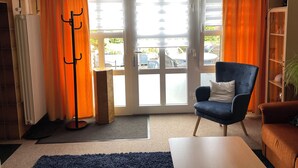 Un salon avec un fauteuil bleu, un canapé marron, une table basse blanche, un lampadaire et une bibliothèque.