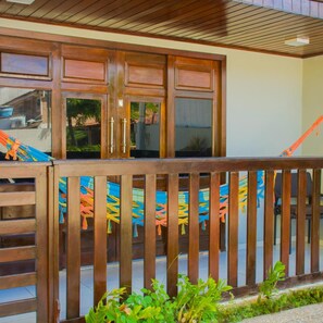 A wooden balcony with a railing, a hammock, and a view of the street. - Pousada Velosmar (Ipojuca)
