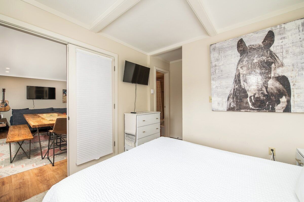 A bedroom with a large bed, a desk with a chair, a television, and a wall-mounted artwork.