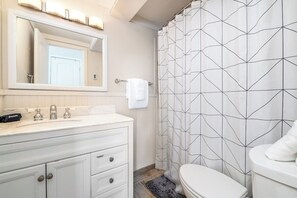 Une salle de bain avec un meuble-lavabo blanc, un miroir, un porte-serviettes et un rideau de douche à motifs géométriques.