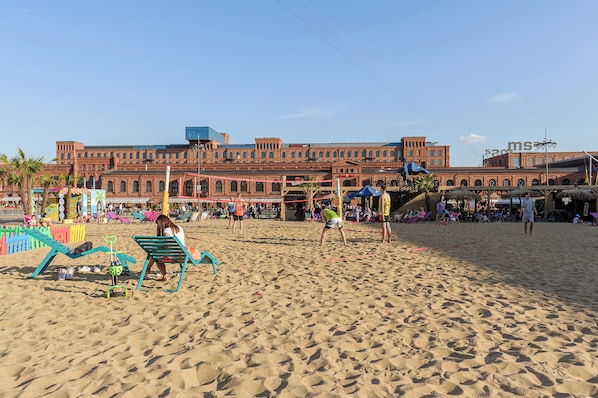 A sandy beach with a large brick building in the background. - Lumina bright apart next to Fabryczna (Lodz)
