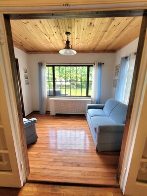 Une pièce avec un plafond en bois, un canapé bleu, une fenêtre avec des rideaux et un radiateur.