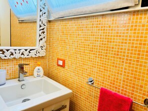 A bathroom with a white sink, a mirror with a decorative frame, and a red towel hanging on a rack. - Bright Apartment With a Lovely Balcony (San Michele al Tagliamento)