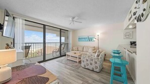 A modern living room with a sofa, coffee table, and a dining area with a table and chairs. There is a balcony with a view of the ocean. - Sea breeze-Steps from the beach (Carolina Beach)