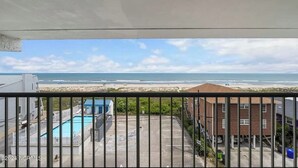 Vista desde un balcón sobre una playa, una piscina y edificios cercanos.