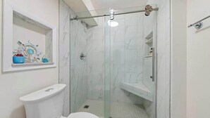 A modern bathroom with a glass-enclosed shower, a toilet, and a shelf with nautical decorations. - Sea breeze-Steps from the beach (Carolina Beach)