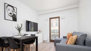 A modern apartment with a dining area, a grey sofa, and a TV mounted on the wall. - Stylish Apartment in Praga | A Place to Work (Warszawa)