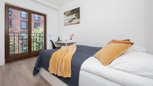 A bedroom with a bed, a desk, and a view of a building through a large window. - Stylish Apartment in Praga | A Place to Work (Warszawa)