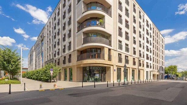 A modern multi-story hotel with a curved facade, balconies, and a clear sky. - Stylish Apartment in Praga | A Place to Work (Warszawa)
