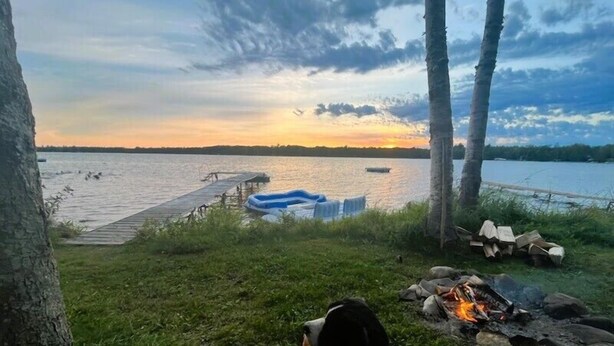 Une vue sur le lac, avec un quai, un bateau et un chien près d’un feu de camp.