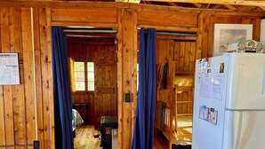 Una baita con pareti in legno, un letto a castello, un frigorifero e una scrivania con una sedia.