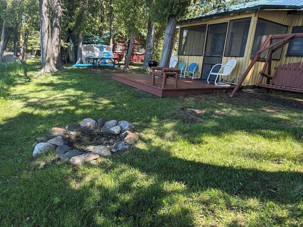 A campsite with a fire pit, outdoor seating, and a screened area. - 1 of 3 beautiful sunset views direct on Birch Lake, water toys, dog ok (Kewadin)
