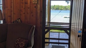 Interno di una baita in legno con vista su un lago attraverso una porta con griglia metallica.