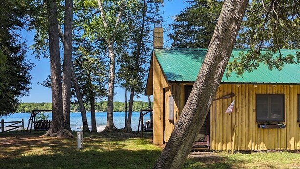 Una baita di legno con tetto verde, situata sulle sponde di un lago, circondata da alberi.