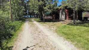 Un chemin de gravier mène à un chalet rustique doté d’un mur en pierre et d’une terrasse en bois.