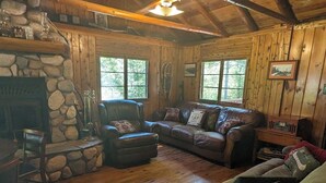 Un intérieur de chalet chaleureux avec une cheminée en pierre, des murs en bois, un canapé en cuir et un coin repas.