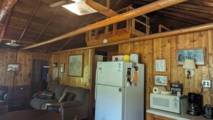 Un intérieur de chalet chaleureux, avec un revêtement mural en bois, un réfrigérateur, un four à micro-ondes, une table à manger et un canapé.