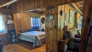 L’intérieur d’une cabane en bois comprend un lit, un lave-linge et une petite table avec une lampe.
