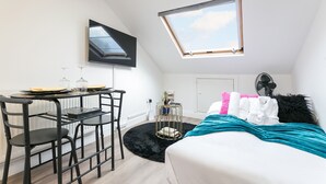 A bedroom with a bed, a desk with a chair, a TV mounted on the wall, a skylight, and a fan. - Cosy 1-bedroom apartment in beautiful location in London with WiFi and Netflix (London)