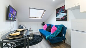 A modern living space with a dining area, a blue sofa with colorful cushions, a skylight, and a large artwork on the wall. - Cosy 1-bedroom apartment in beautiful location in London with WiFi and Netflix (London)
