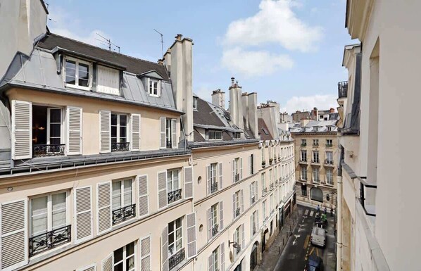A narrow street with multi-story buildings, featuring balconies and shutters.