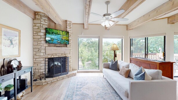 A living room with a stone fireplace, a white couch, and a large window with a view of trees. - River City Resorts: RPS 104: River View Condo! Free Tubes Included! (New Braunfels)