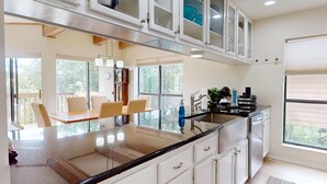 A modern kitchen with white cabinets, a black countertop, and a dining area with chairs. - River City Resorts: RPS 104: River View Condo! Free Tubes Included! (New Braunfels)