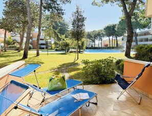 Zona de piscina con sillas de descanso, un bolso verde y vista despejada a la piscina y la vegetación circundante.