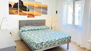 A modern bedroom with a bed, a bedside table, a lamp, a window with curtains, and a wall with a sunset painting.