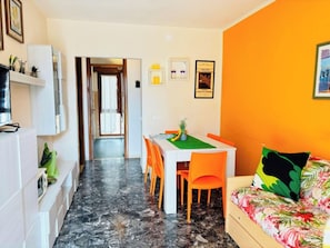 Un espacio habitable compacto con comedor, un sofá tapizado con motivos florales y un pasillo que conduce a otra habitación.