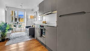 Eine moderne Küche mit Edelstahlgeräten, ein Essbereich mit Tisch und Stühlen sowie ein Blick ins Freie durch große Fenster.