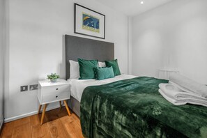 A neatly arranged bedroom with a bed, a nightstand, a framed picture on the wall, and a radiator. - Classic One Bedroom Apartment in Camden (London)