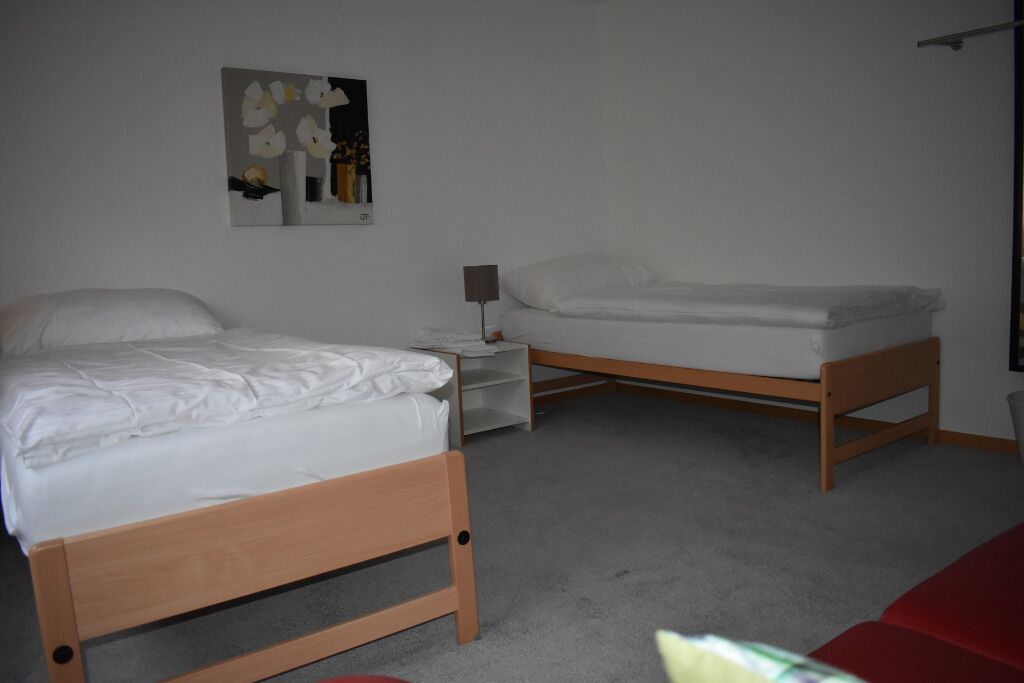 A bedroom with two single beds, a bedside table with a lamp, and a wall-mounted artwork.