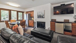 Ein modernes Wohnzimmer mit einer Ledersofa, einem Essbereich mit Holzsesseln, einer Küche mit Holzschränken und einem an der Wand befestigten Flachbildfernseher.